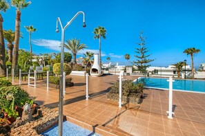 A pool area with a tiled deck, palm trees, and a clear blue sky.