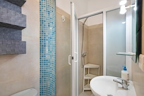 A bathroom with a glass shower enclosure, a white sink, and a blue-tiled column.