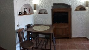 A dining area with a round table, chairs, a wooden cabinet, and white textured walls.