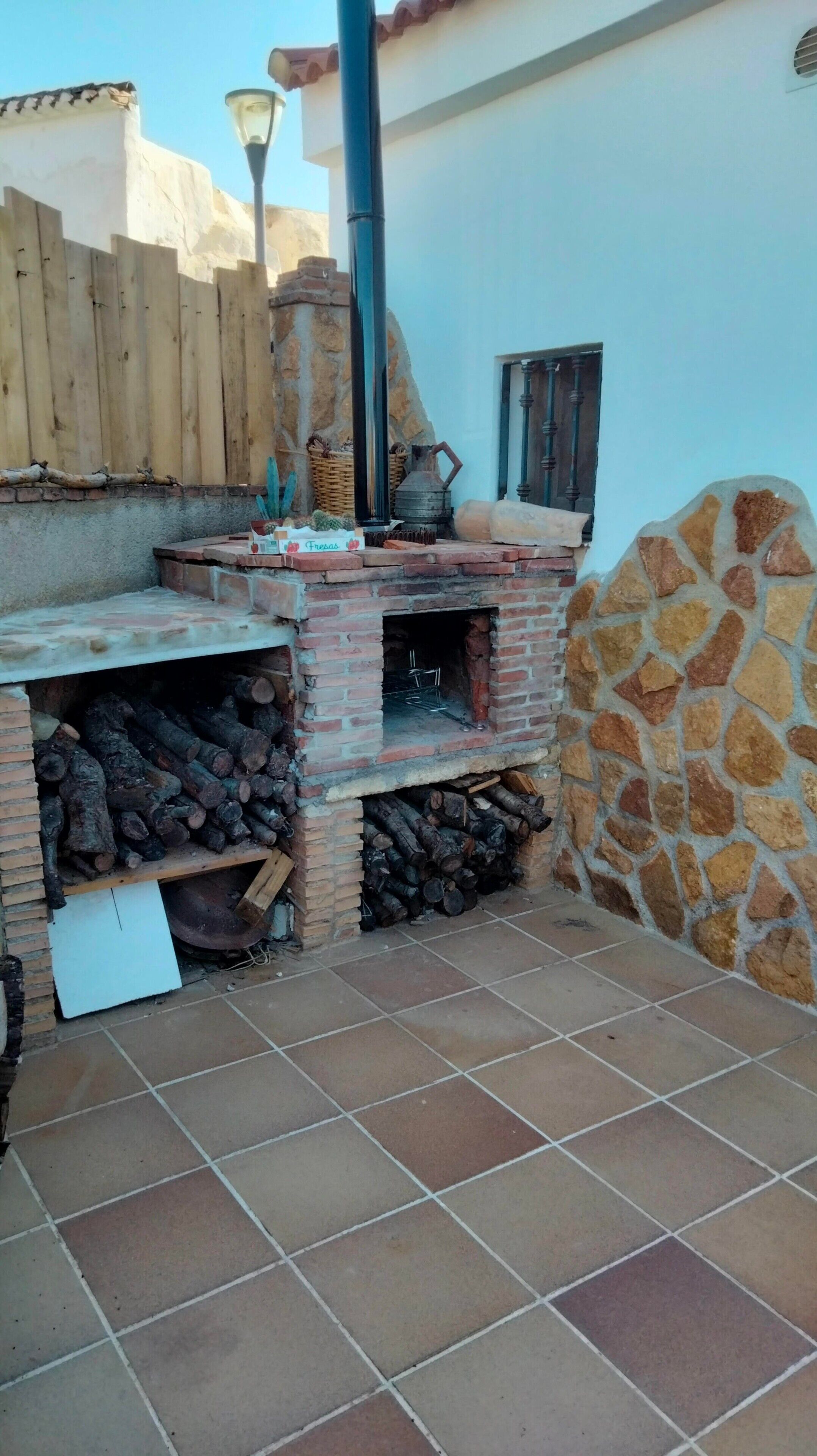 Un horno de ladrillo con una chimenea, una valla de madera y un muro de piedra.