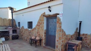 A patio area with a stone wall, a wooden bench, a table, a door, and a chimney.