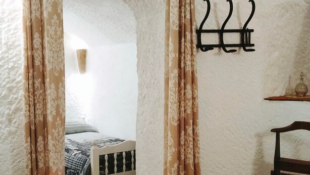 A room with a bed, a chair, a table, and a wall-mounted coat rack.