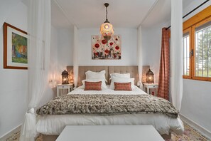 A bedroom with a large bed, two bedside tables, a chandelier, and artwork on the walls.