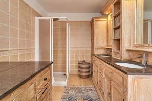 A bathroom with wooden cabinets, two sinks, a shower, and a patterned rug.