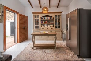 Een keuken met een houten tafel, een inbouwboekenplank, een koelkast en een hanglamp.