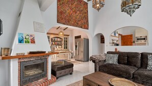 Uma sala de estar com lareira, sofá, mesa de centro e cozinha ao fundo.
