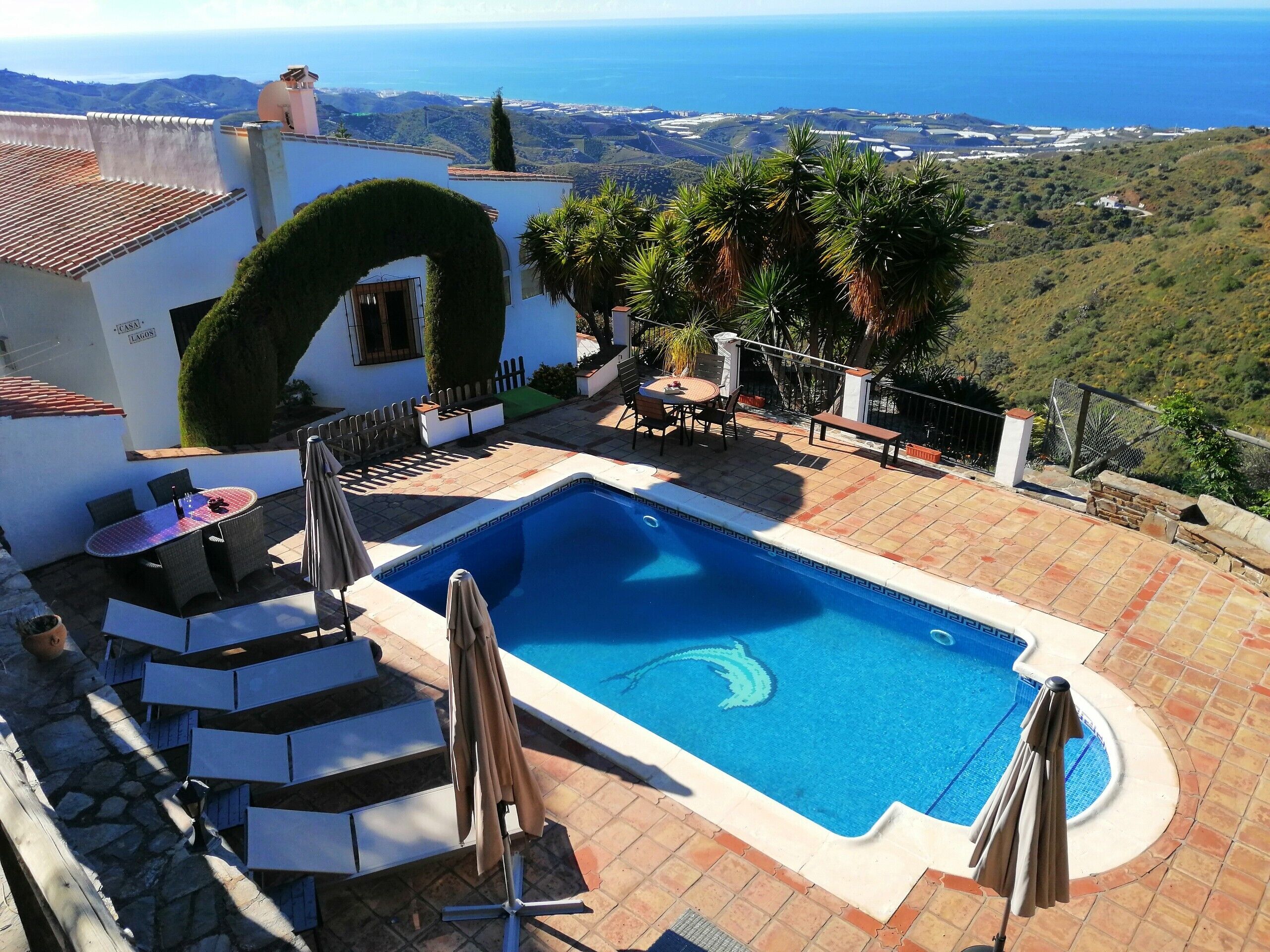 A swimming pool with a view of the sea, surrounded by a patio with chairs and umbrellas.