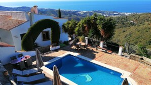 Piscina com vista para o mar, rodeada por um terraço com cadeiras e guarda-sóis.