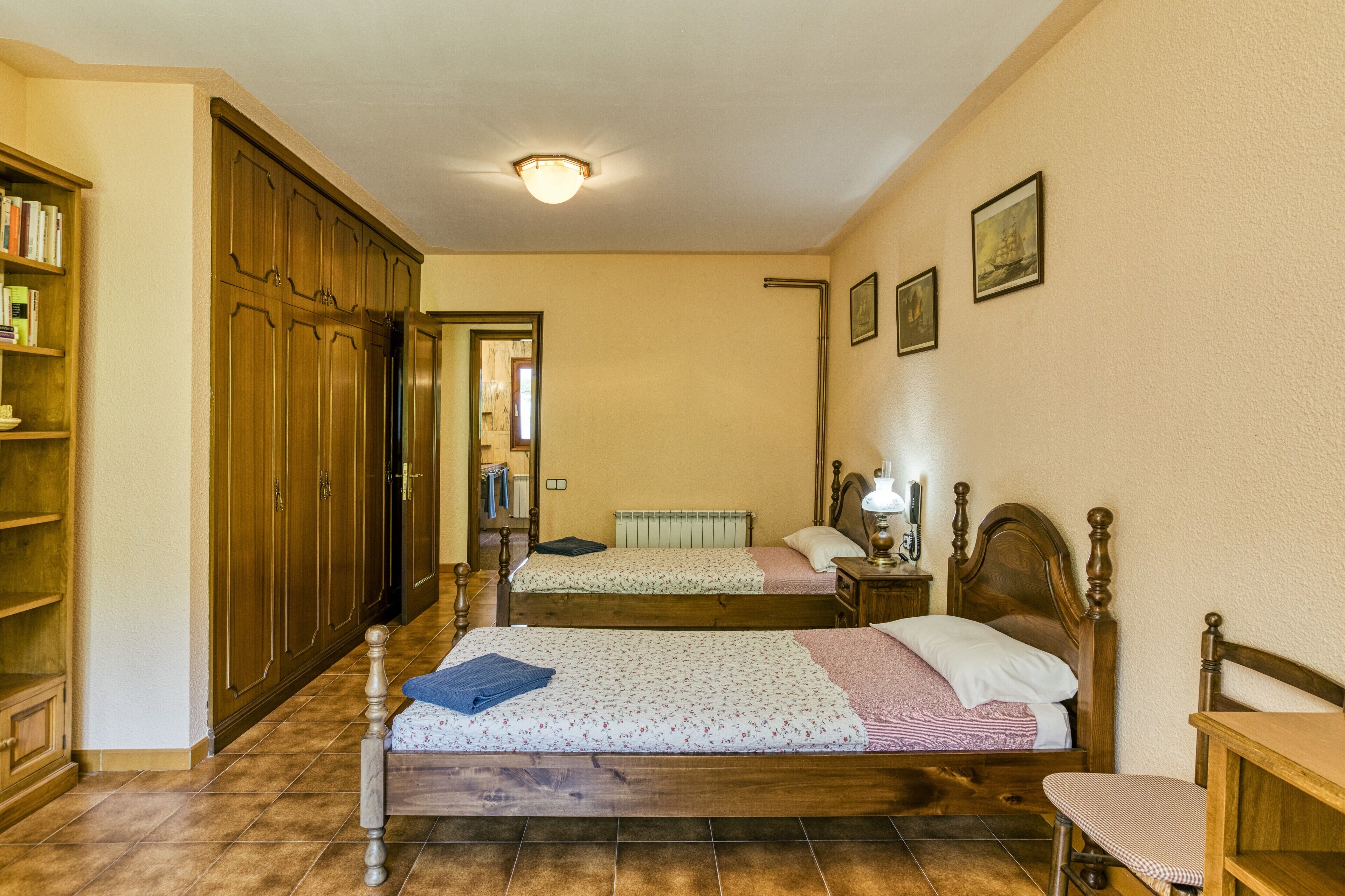 A bedroom with two beds, wooden furniture, a bookshelf, and a ceiling light.