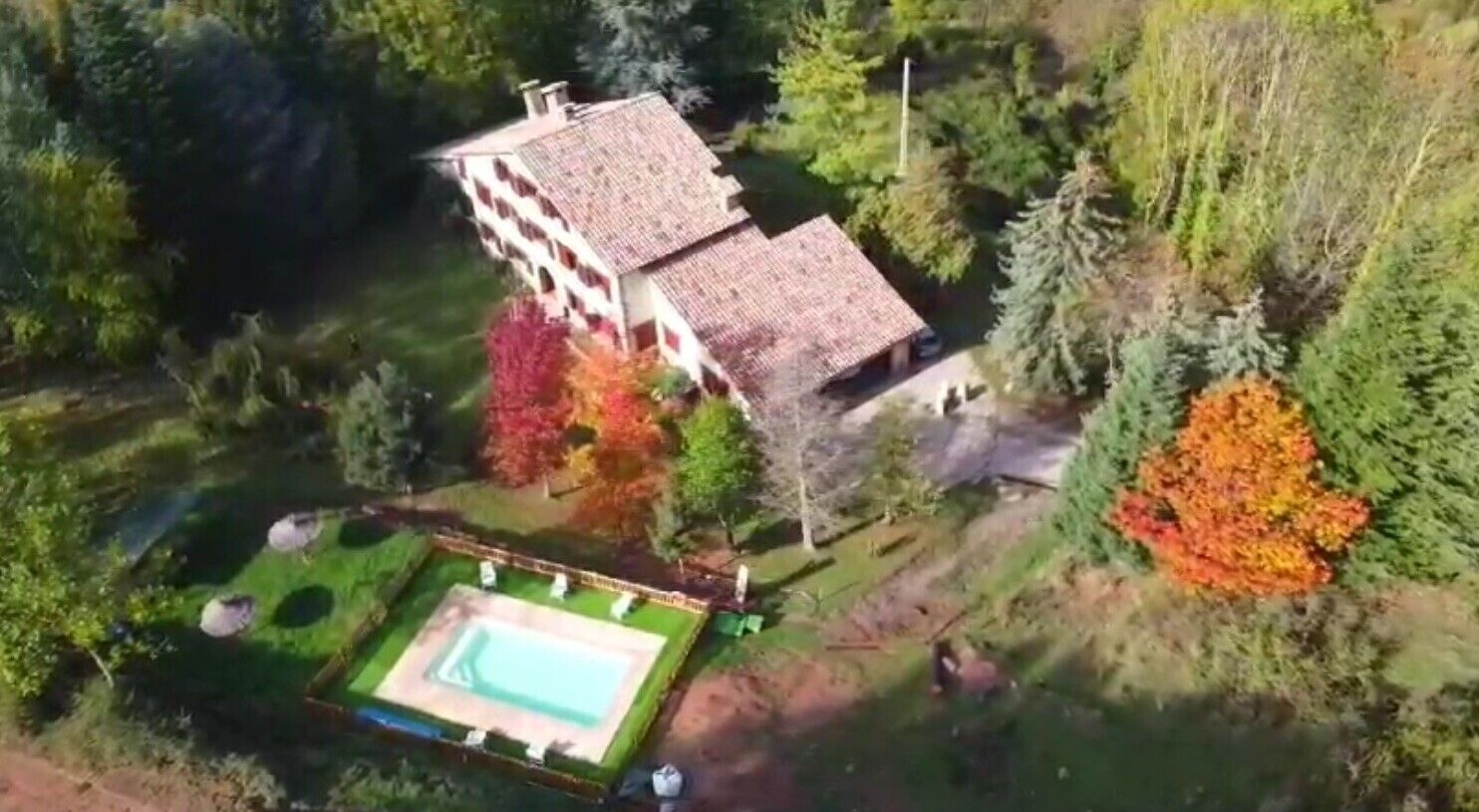 Un edificio grande con piscina, rodeado de árboles y follaje.