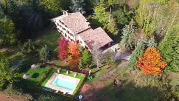 Un edificio grande con piscina, rodeado de árboles y follaje.