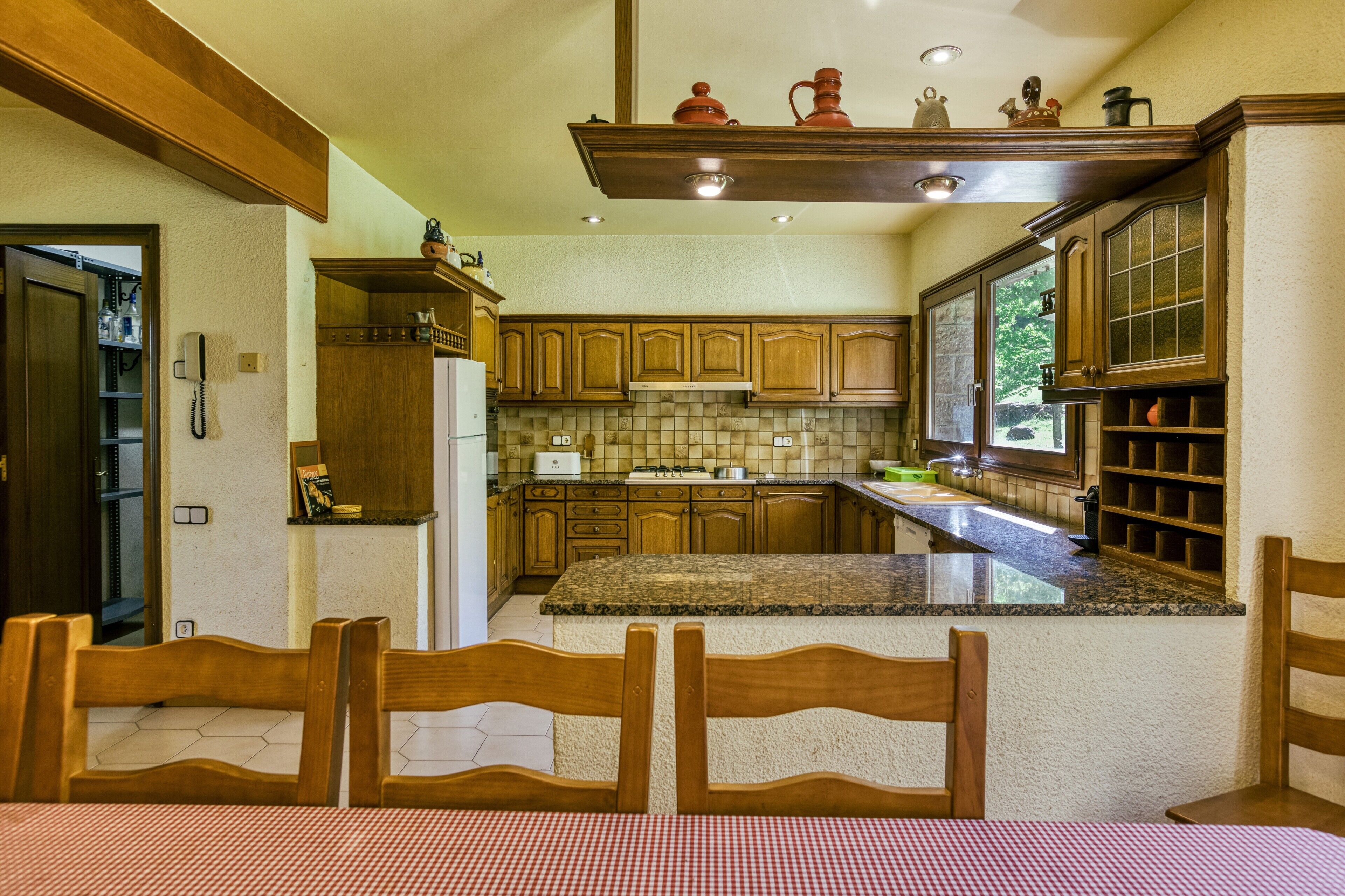 Una cocina con armarios de madera, encimera de granito y una zona de comedor con mantel a cuadros.