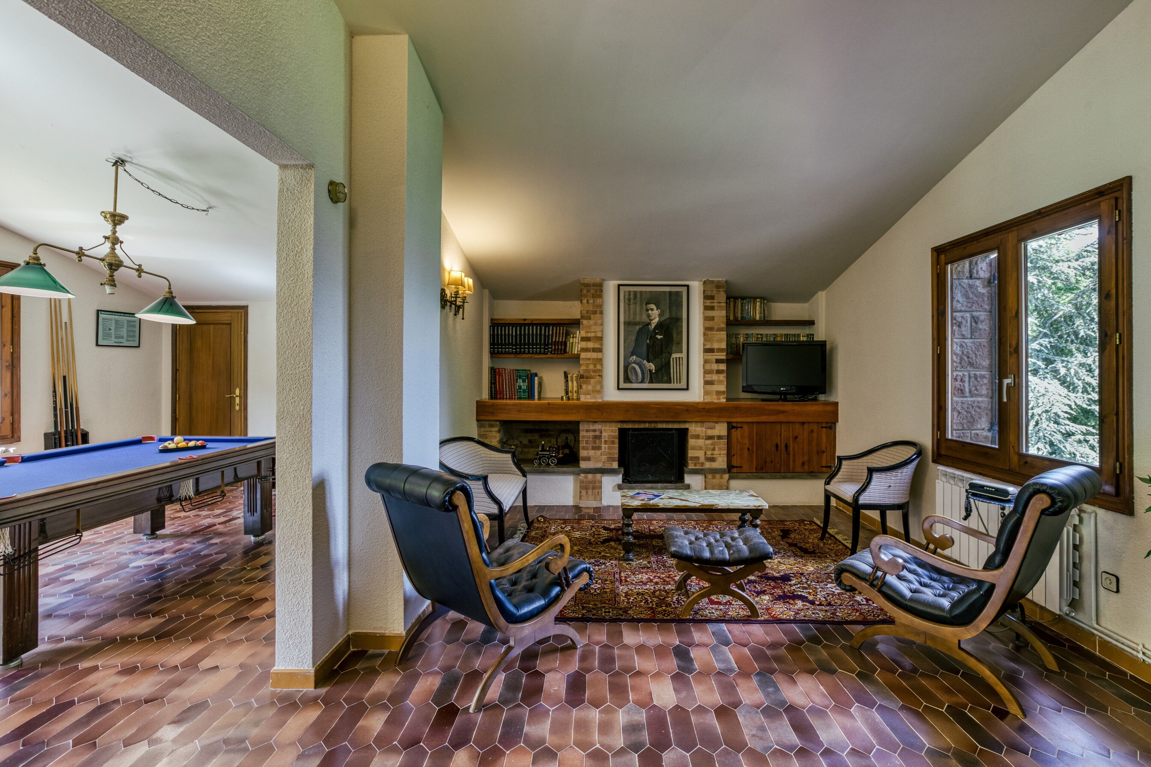 Una mesa de billar, dos sillones de cuero, una chimenea y un televisor en una sala de estar con piso de ladrillo.