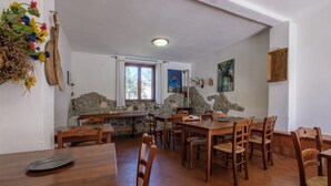 A dining area with wooden tables and chairs, a stone wall, and a window with curtains.
