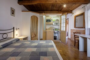 Une chambre à coucher comprenant un lit, une table de chevet, un plafond en bois et une porte ouverte donnant sur un coin cuisine équipé d’un évier et de placards.