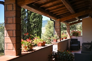 Un espacio de estar al aire libre con techo, columnas de ladrillo, plantas en macetas y vistas a árboles y montañas.