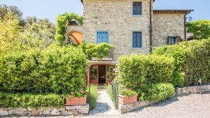 Un edificio in pietra con un ingresso centrale, un balcone al secondo piano e un piccolo giardino.