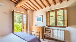 Una camera da letto con un letto, una cassettiera in legno, una sedia, una finestra, un termosifone e un quadro appeso al muro.