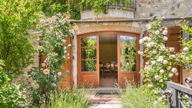 Un edificio in pietra con una porta in legno e un piccolo giardino con rose.
