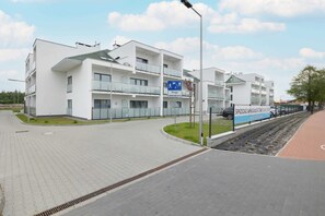 A modern multi-story building with balconies, a paved area, and a sign indicating a drop-off zone. - Family Apartment with Terrace | 2 Bedrooms and Parking (Grzybowo)