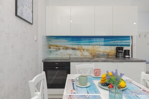 A modern kitchen with white cabinets, a large backsplash, and a dining area with a table set for two. - Family Apartment with Terrace | 2 Bedrooms and Parking (Grzybowo)