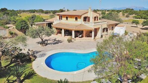 Une maison à deux étages avec une piscine, entourée de verdure et sous un ciel dégagé.