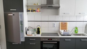 A modern kitchen with grey cabinets, a built-in oven, and a stainless steel refrigerator.