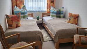 A room with two beds, a small table, a chair, and a window with curtains.