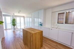A modern kitchen with white cabinets, a wooden island, and a large window with blinds.