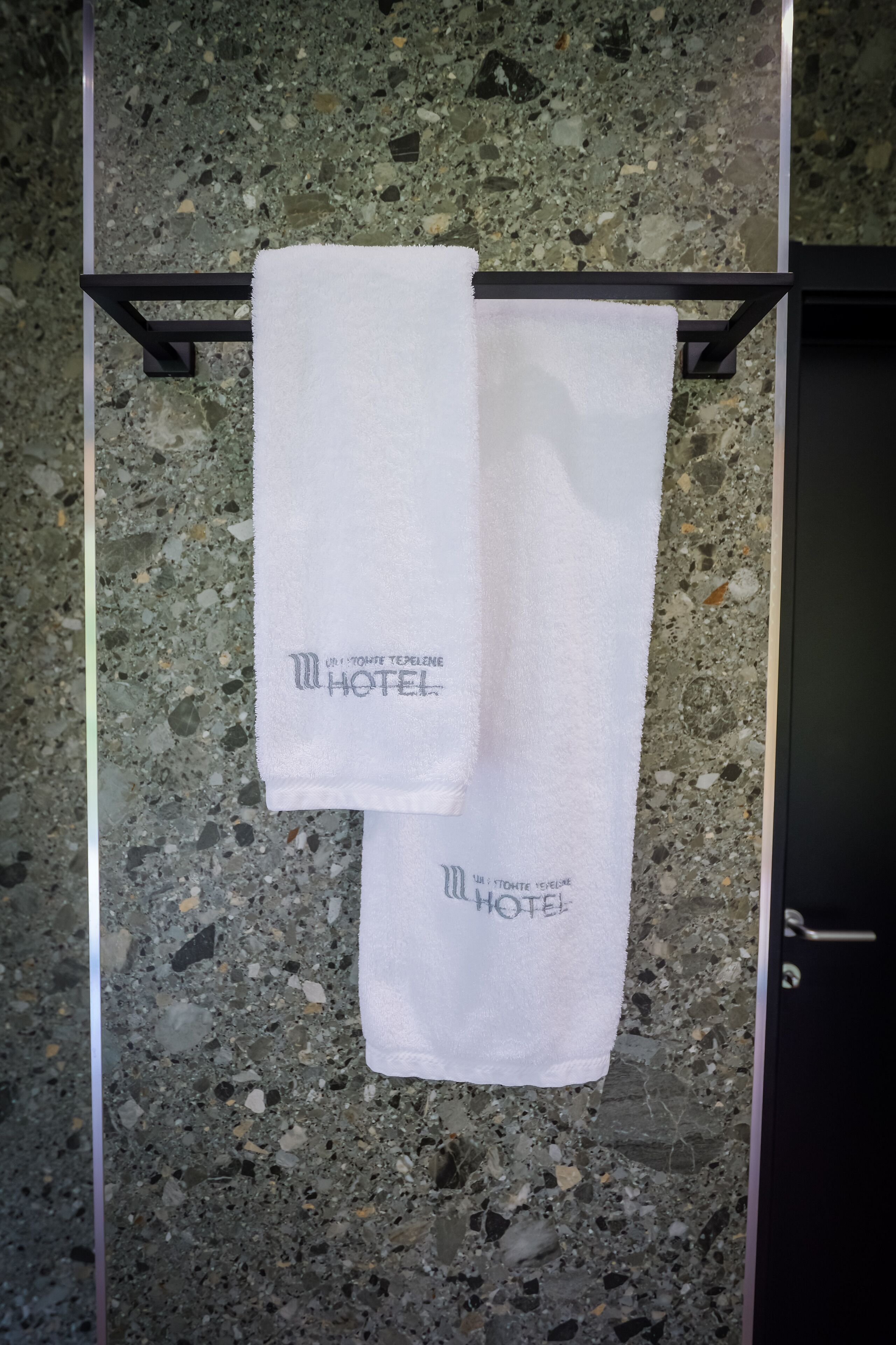 Deux serviettes blanches sont suspendues à un étendoir en métal, devant un sol en terrazzo.