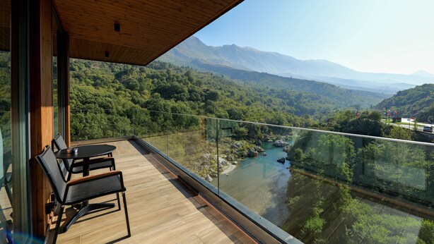 A balcony with wooden flooring and black chairs, overlooking a river and mountains. - Uji i Ftohte Hotel (Qendër Tepelenë)