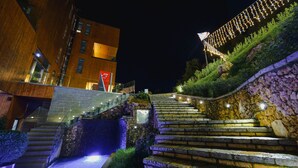 A staircase leading up to a building with a stone wall and a sign for an ATM. - Uji i Ftohte Hotel (Qendër Tepelenë)