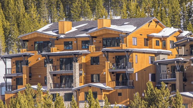 A multi-story wooden lodge with balconies, large windows, and a snowy landscape in the background.