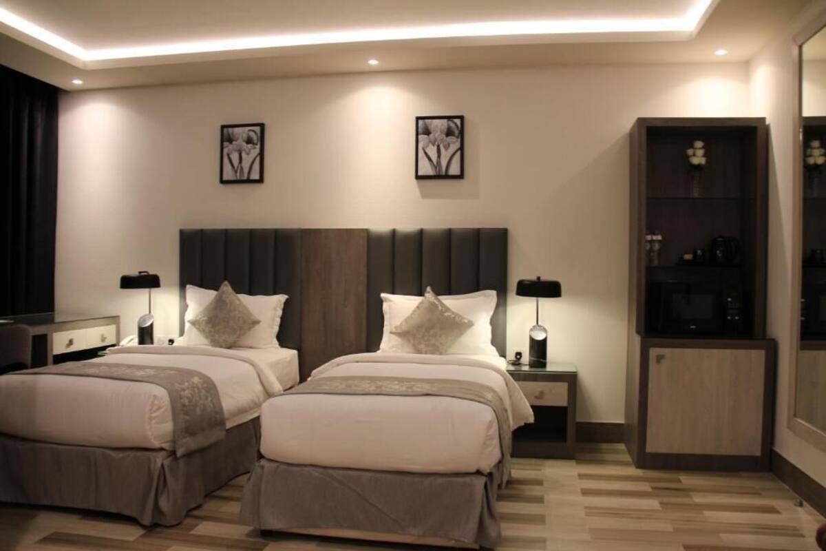 Ein modernes Hotelzimmer mit zwei Betten, einem integrierten Kleiderschrank und einer kleinen Küchenzeile.