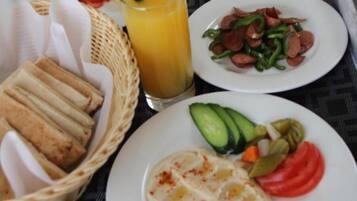 Una bandeja con diversos alimentos para desayuno, incluyendo tostadas, un tazón de sopa, un plato con tomates y pepinos en rodajas, un vaso de jugo de naranja y un plato con salchichas y pimientos.
