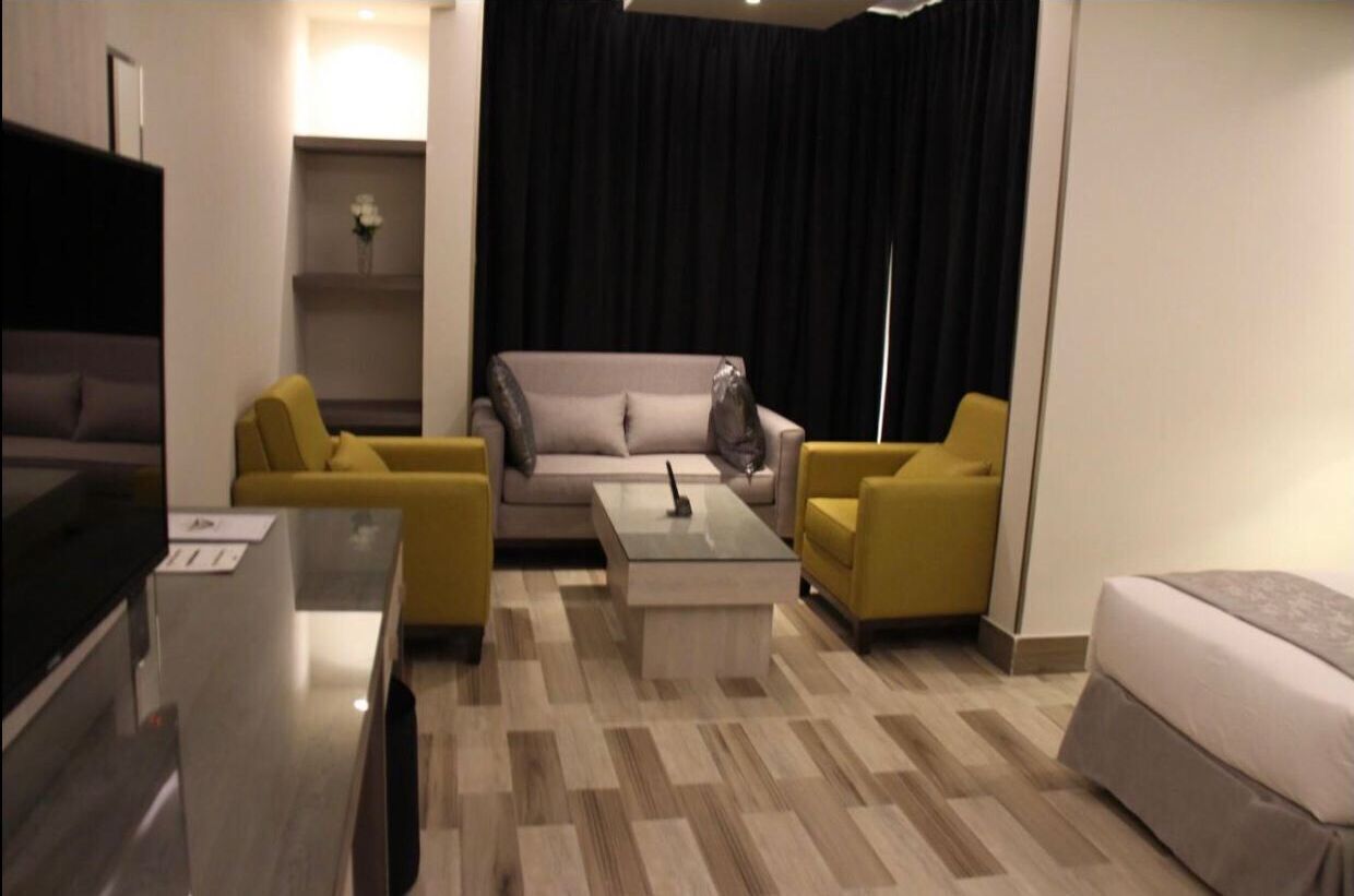 Ein modernes Hotelzimmer mit einer Couch, zwei Sesseln, einem Couchtisch und einem Fernseher.