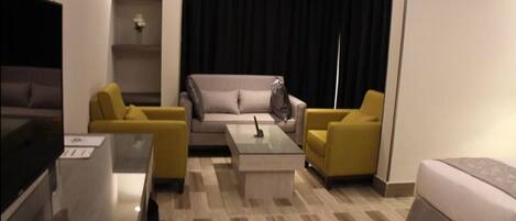 Ein modernes Hotelzimmer mit einer Couch, zwei Sesseln, einem Couchtisch und einem Fernseher.