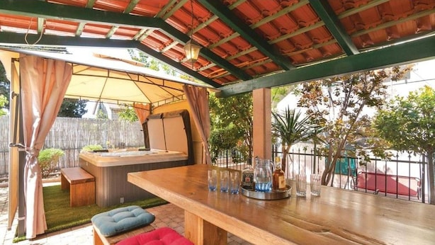 Una terrazza esterna con tavolo in legno, sedute imbottite e un angolo bar con bicchieri e bottiglie.