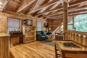 Cozy cabin interior with a high ceiling, wooden beams, and a dark leather sofa.