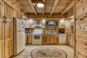 Kitchen features a central island, refrigerator, stove, and dishwasher, with exposed wooden beams and a central light fixture.