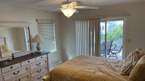 Una camera da letto con un letto, una cassettiera, un ventilatore a soffitto e vista all'esterno tramite una porta scorrevole in vetro.