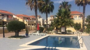 A swimming pool with a hot tub, surrounded by palm trees and a building with red-tiled roofs.