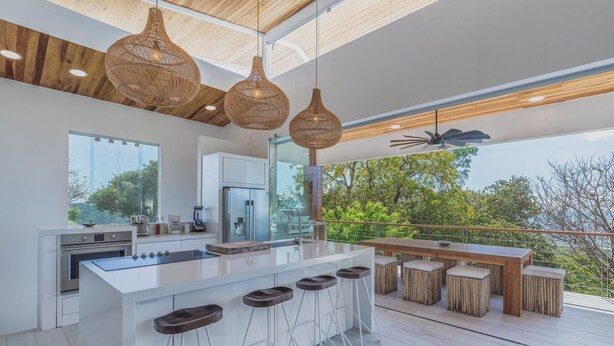 A modern kitchen with a large island, bar stools, and a dining area with a wooden table and benches.