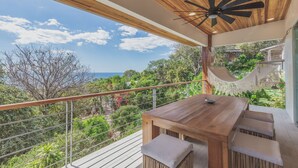 A wooden deck with a table and benches overlooking a lush garden and ocean view.
