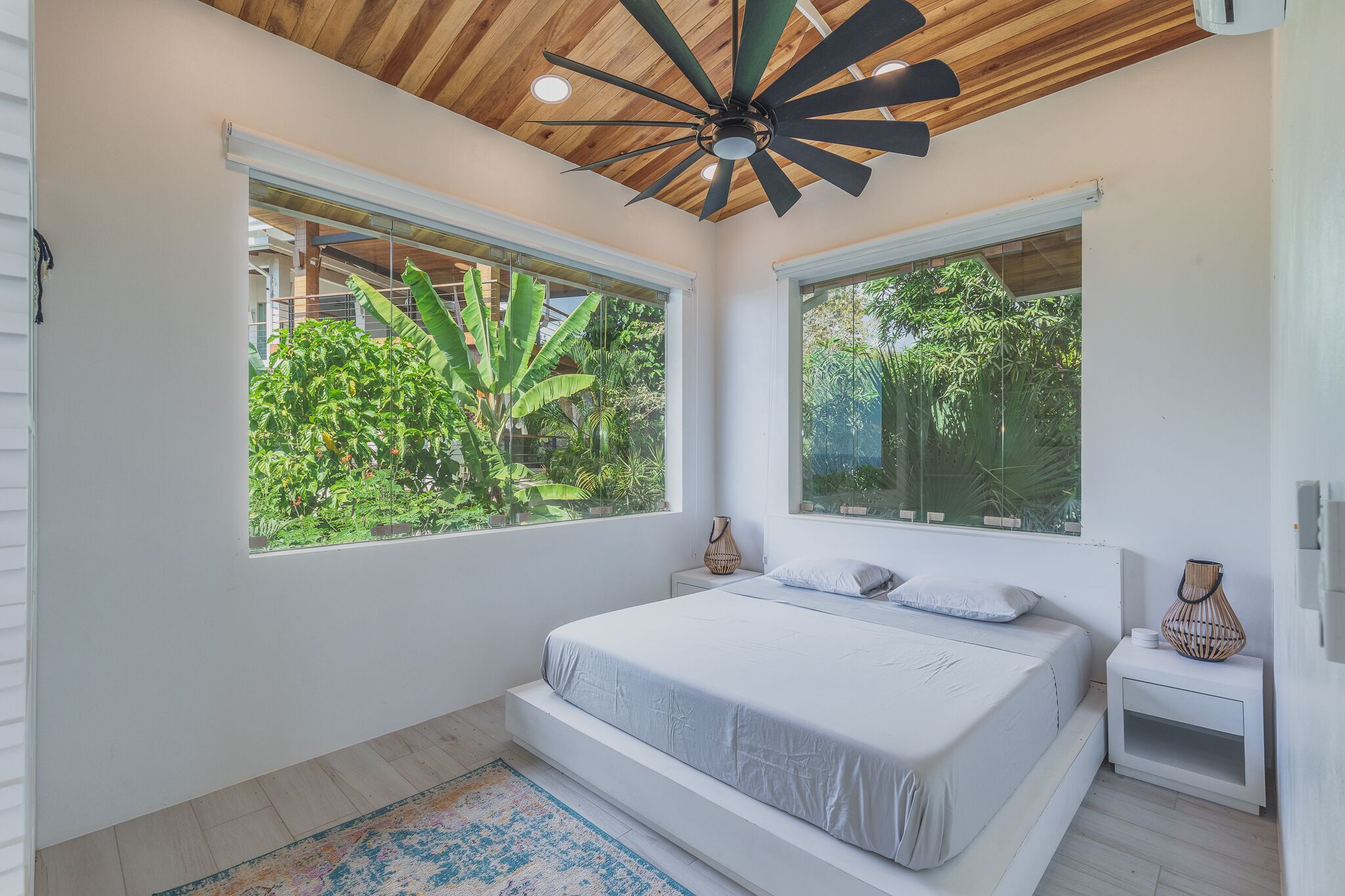 A bedroom with a bed, two windows, a ceiling fan, and a nightstand.