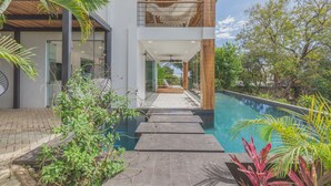 A modern house with a pool, a covered walkway, and lush greenery.