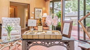 Una habitación con una mesa de vidrio que muestra una botella de vino, un cartel de bienvenida enmarcado y una bandeja con aperitivos.