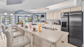 Une cuisine moderne dotée d’un grand îlot central, d’appareils électroménagers en acier inoxydable et offrant une vue sur l’extérieur.