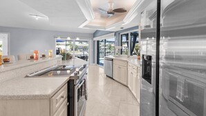 Une cuisine moderne dotée d’un grand îlot central, d’appareils électroménagers en acier inoxydable et offrant une vue sur l’extérieur.