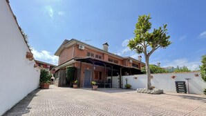 Een huis met twee verdiepingen, een betegeld terras, een boom en een poort.